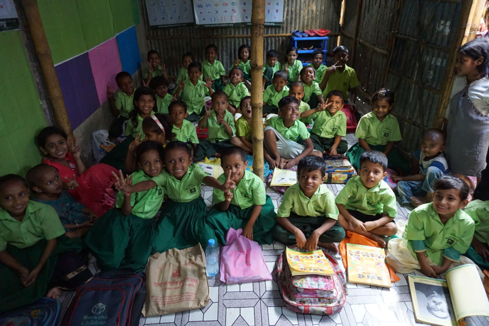 Children in green school uniforms sit in a classroom and post for a photo.