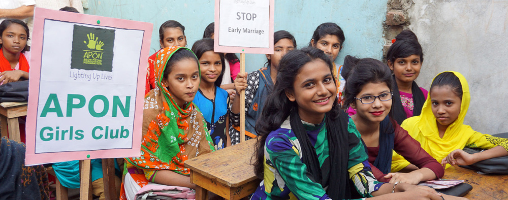 Bangladeshi girls sit at desks and hold signs protesting child marriage