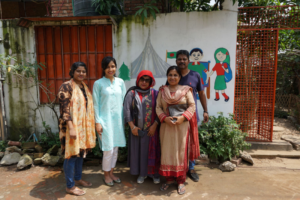 GFC and LEEDO staff stand outside against a white wall with paintings of children. © Global Fund for Children