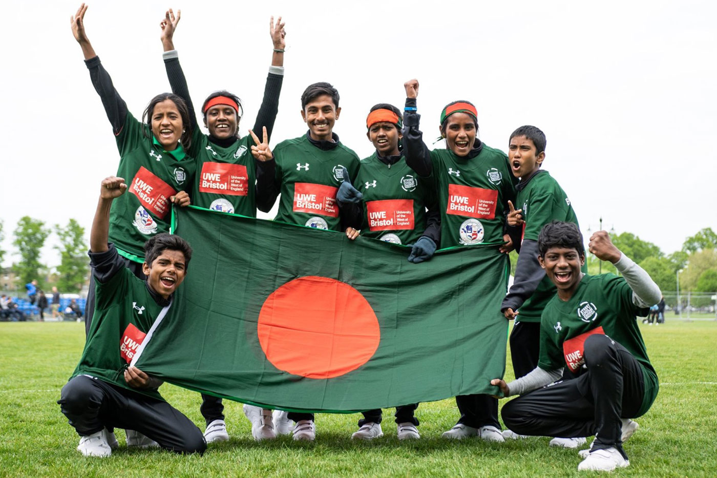LEEDO's Street Child Cricket World Cup team members stand outside holding the flag of Bangladesh and raising their hands in victory. © LEEDO