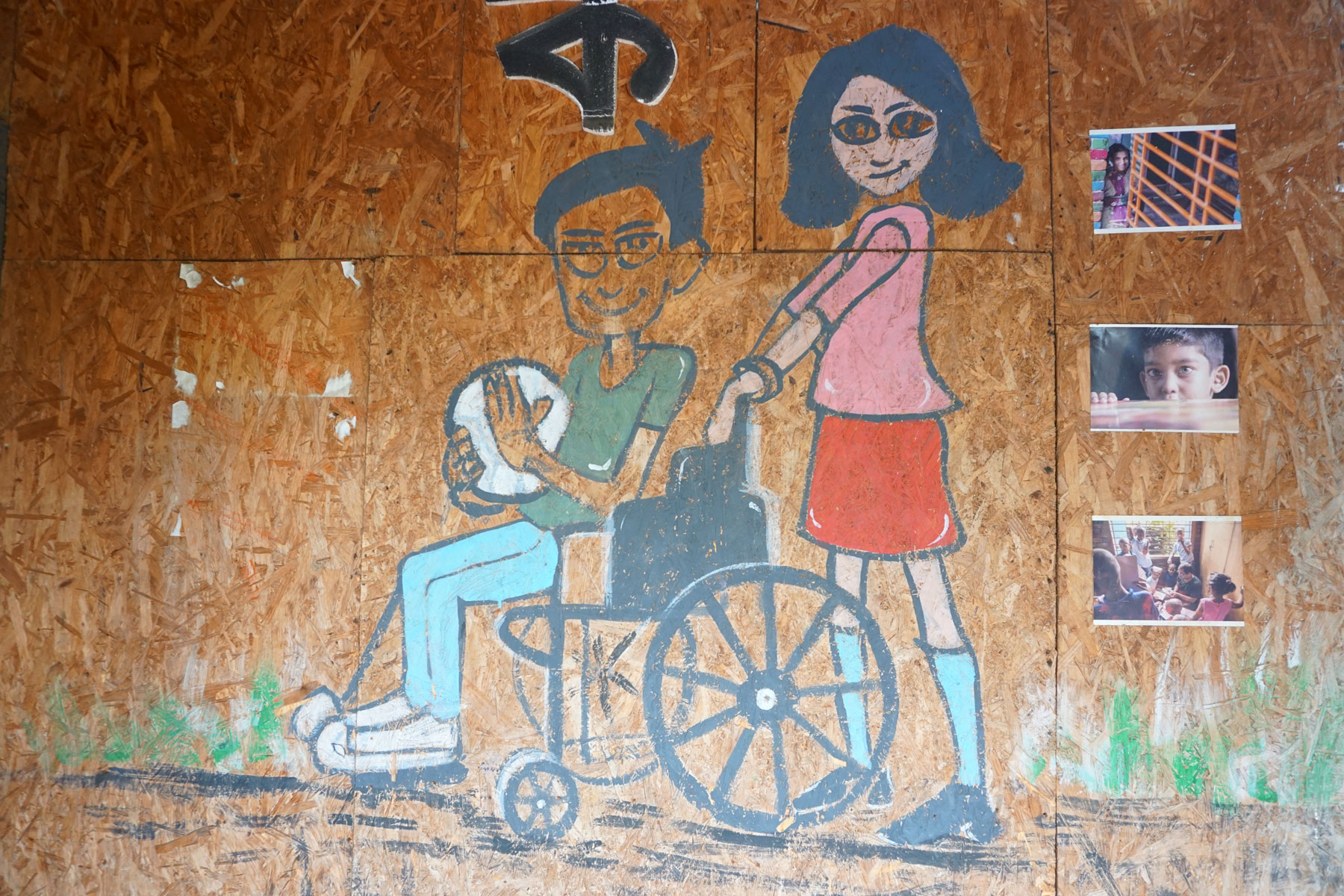A plywood wall painted with a girl pushing a boy in a wheelchair. © Global Fund for Children