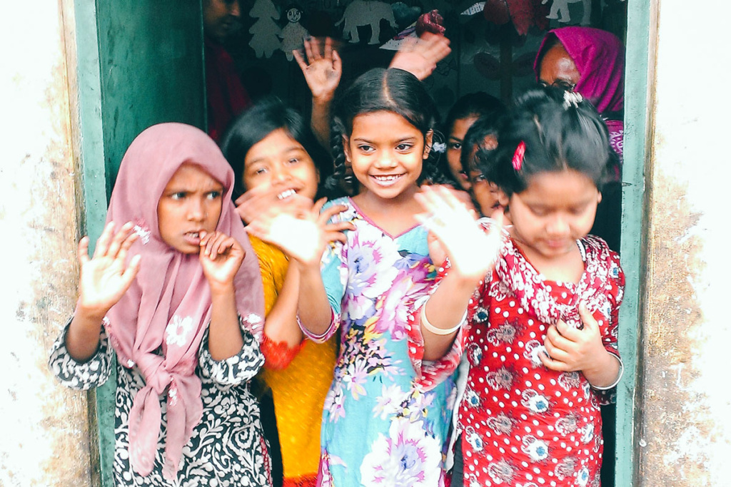 Four girls smile and wave as they exit a building.