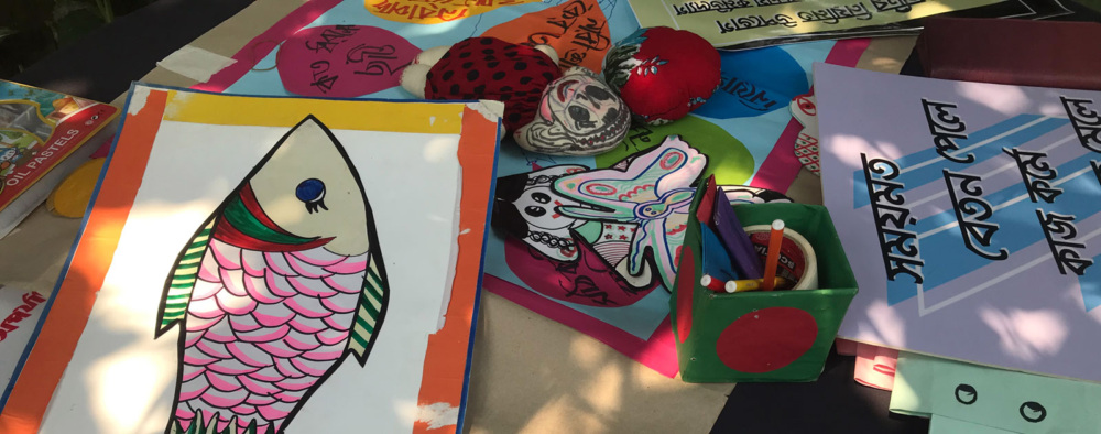 Pastels, dolls, and educational posters in Bengali on a table.