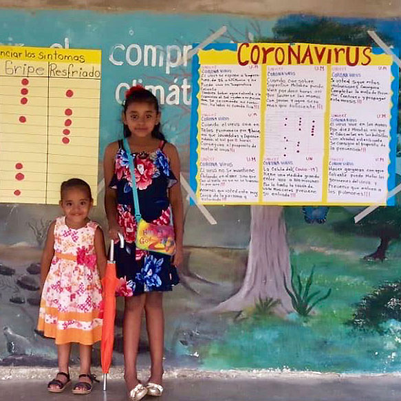 A woman and two children stand in front of posters with information about coronavirus.