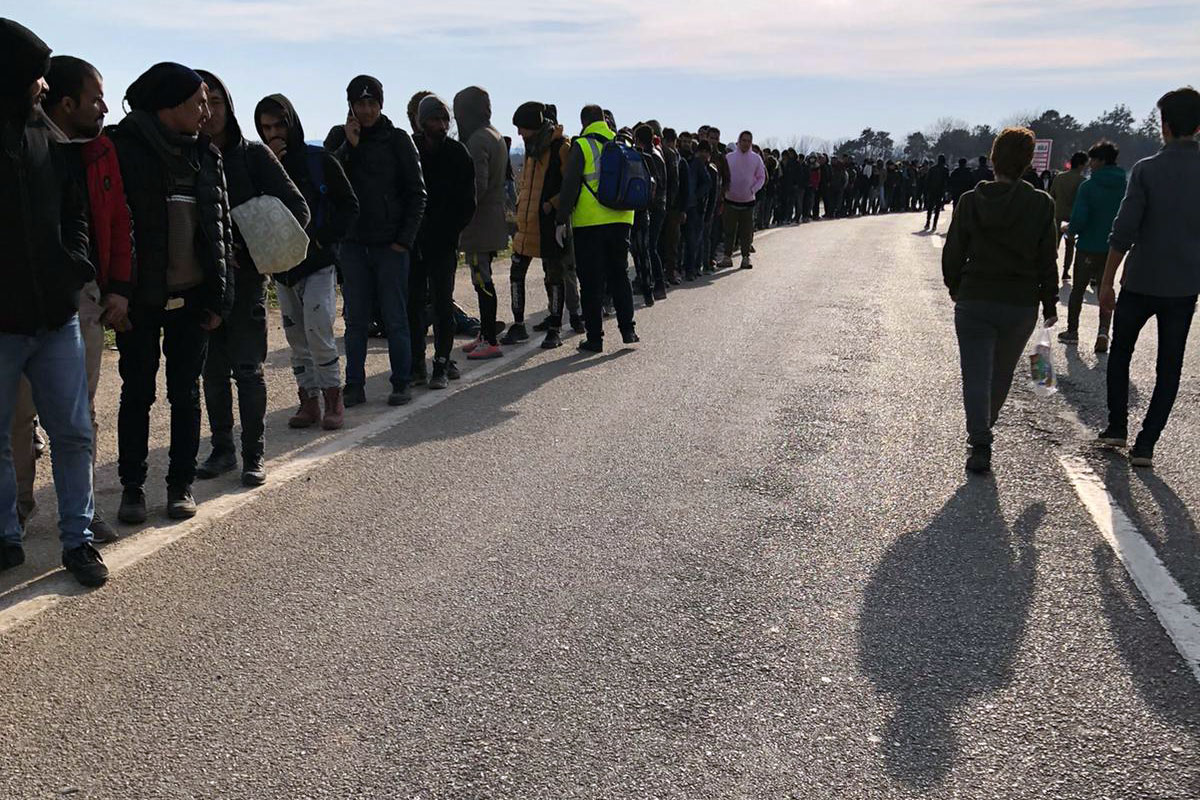 A large group of people stand in line along an asphalt road.