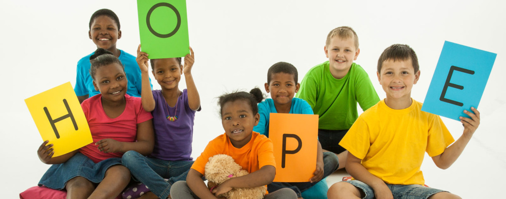 Seven children hold up colored paper with letters that spell the word HOPE.