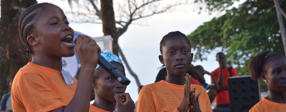 A group of young women gather outside, and one youth leader speaks into a microphone