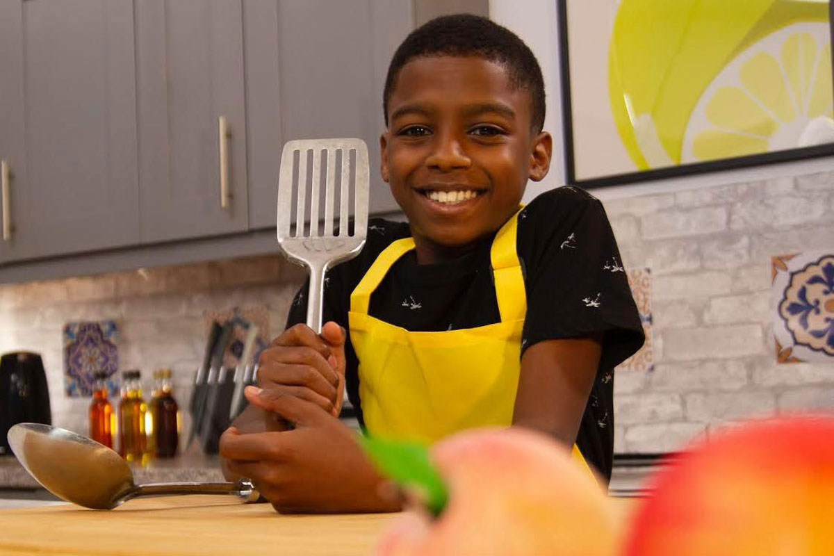 Omari McQueen stands in the kitchen holding a spatula.