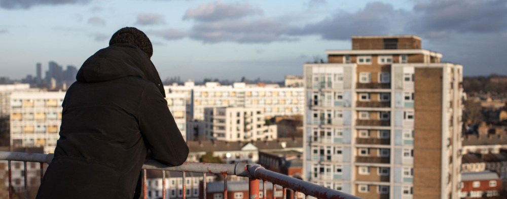 Cyrus on a balcony overlooking apartment buildings.