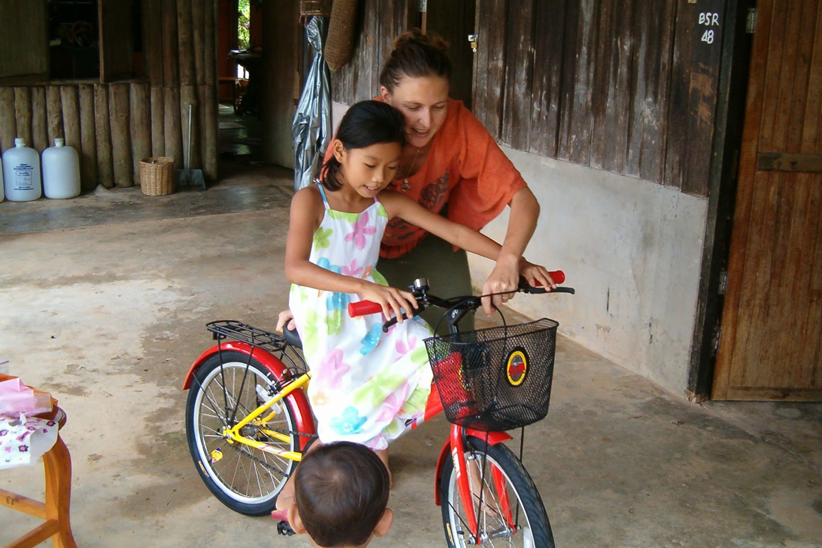 Rosalie helps a child at TCDF's Forest School Academy learn to ride a bike.