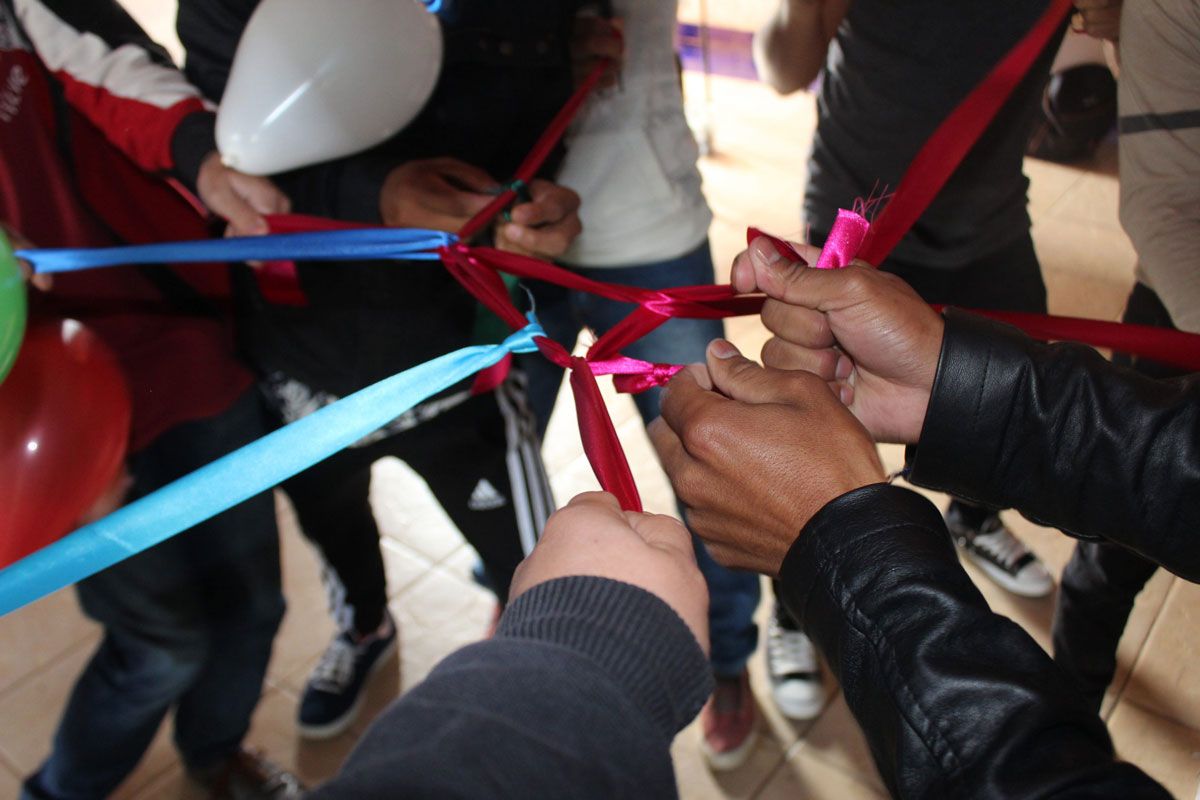 Hands of young men holding a series of interconnected ribbons.