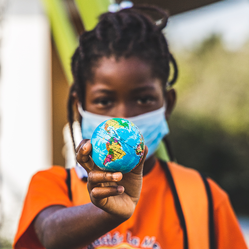 During the pandemic, young person holds small globe in their hand.