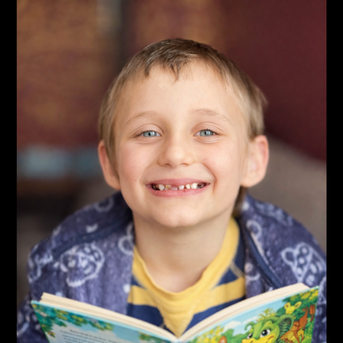 A little boy reading a book but smiling at the camera