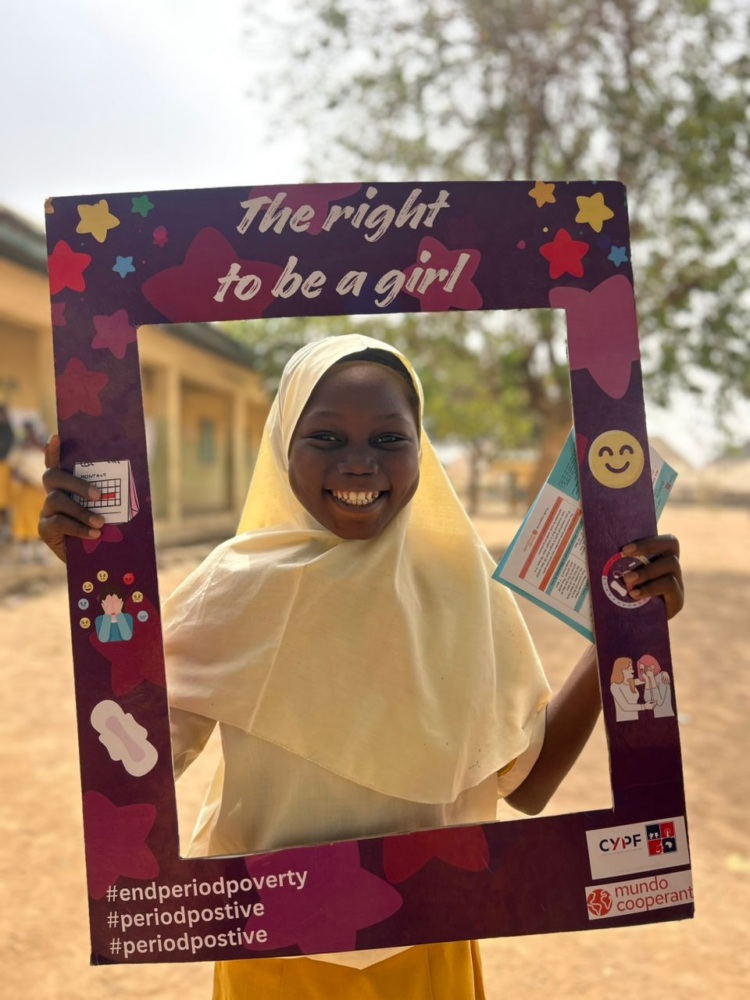 A girl holding a cut out photo frame which says "the right to be a girl"